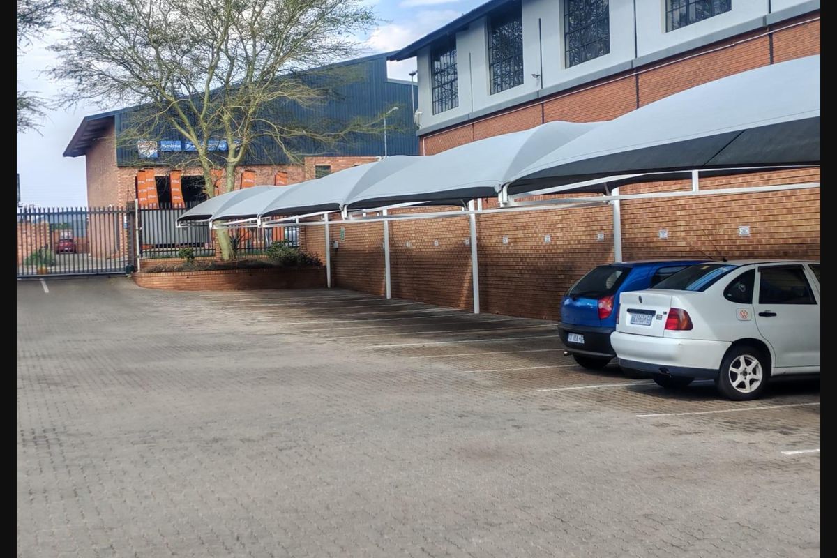 Commercial parking area featuring multiple shade cloth carports, paved surfacing, and secure perimeter brick walling with industrial-style building architecture.