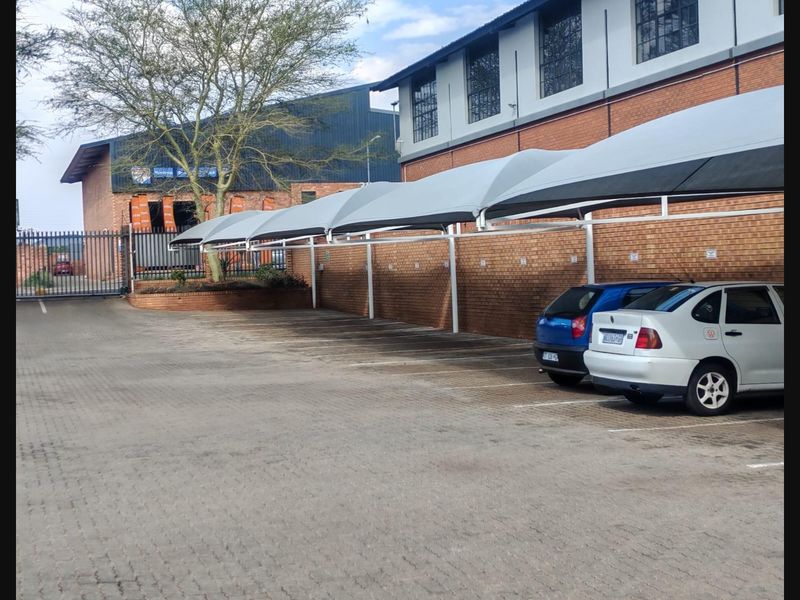Commercial parking area featuring multiple shade cloth carports, paved surfacing, and secure perimeter brick walling with industrial-style building architecture.