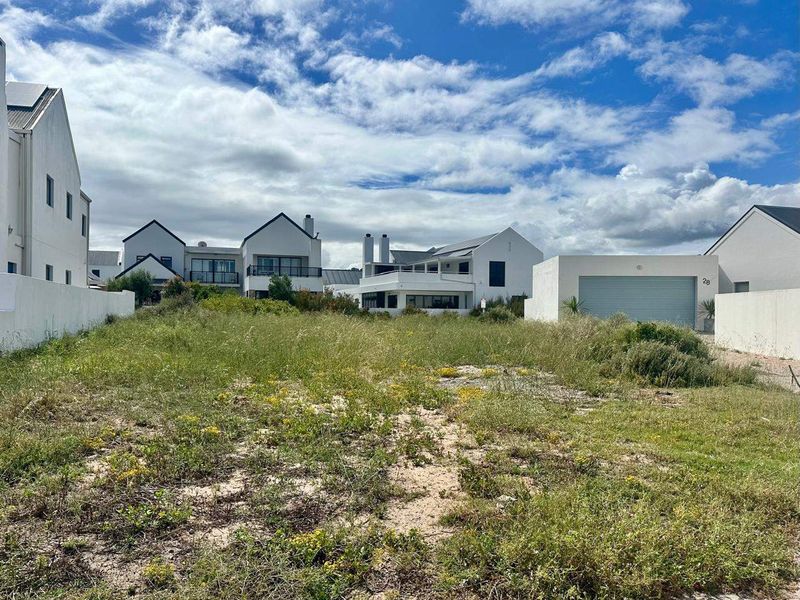 A vacant residential plot situated in a developed estate, featuring boundary walls and adjacent garage access.
