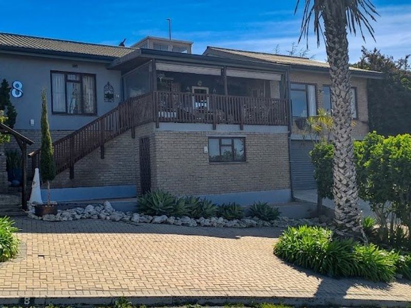 Front elevation of a multi-level house featuring a paved driveway, raised wooden deck with staircase, and a combination of brick and rendered wall finishes.