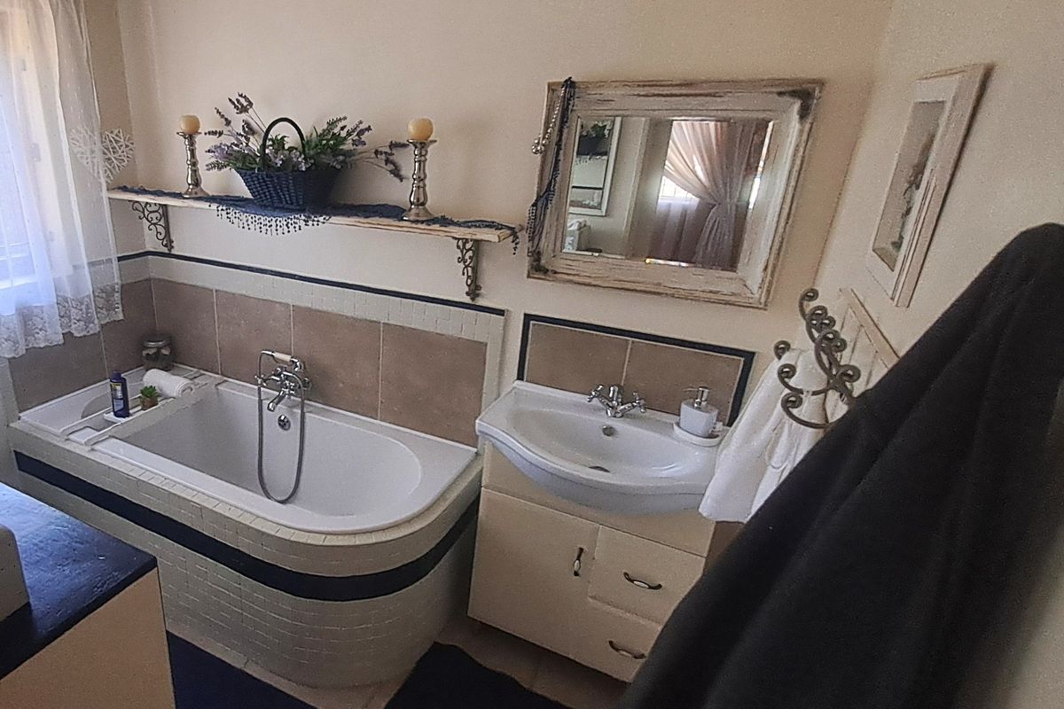 A functional bathroom featuring a built-in bathtub with tiled surround, a vanity cabinet with basin, and wall-mounted shelving.