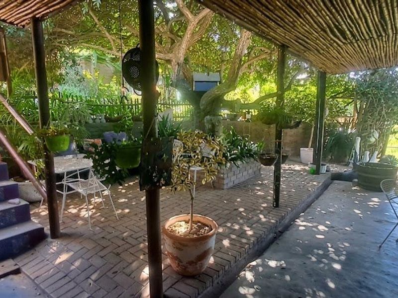 A covered outdoor patio area featuring brick paving, a thatched roof structure, and a tiled staircase leading to the garden.