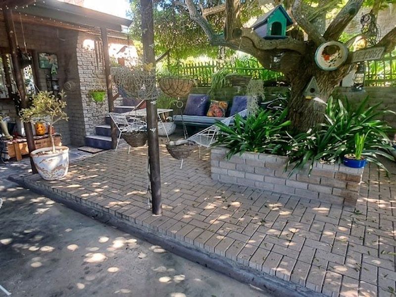 A shaded outdoor patio area featuring brick paving, a built-in planter box, and a mature tree, providing a cozy space for outdoor relaxation.