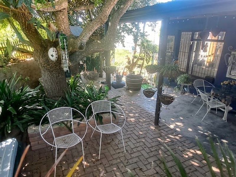 A shaded outdoor patio area featuring brick paving, established trees, and direct access to the home through a security gate.
