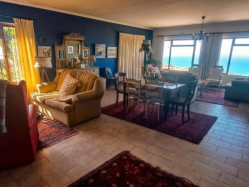 Spacious open-plan living and dining area featuring tiled floors, large windows with ocean views, and direct access to outdoor space.