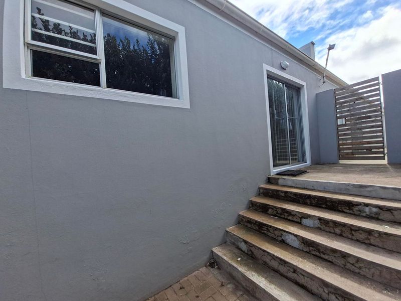 Rear exterior view of the apartment featuring a sliding glass door, concrete staircase, and a timber slat gate.