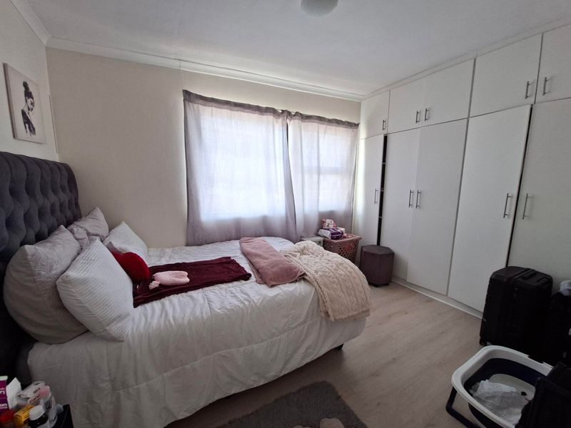 A well-maintained bedroom featuring light laminate flooring, neutral walls, and extensive floor-to-ceiling built-in cupboards for ample storage.