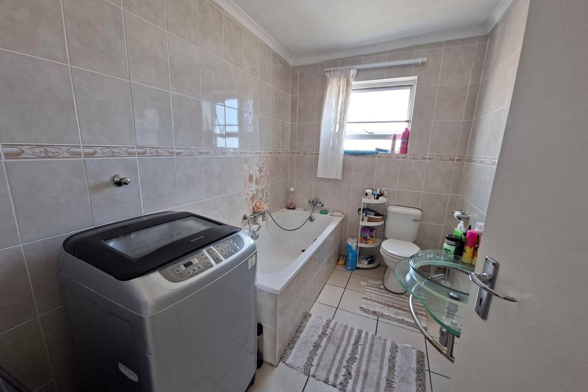 A functional bathroom featuring a bathtub, toilet, and glass basin with neutral ceramic wall and floor tiling.