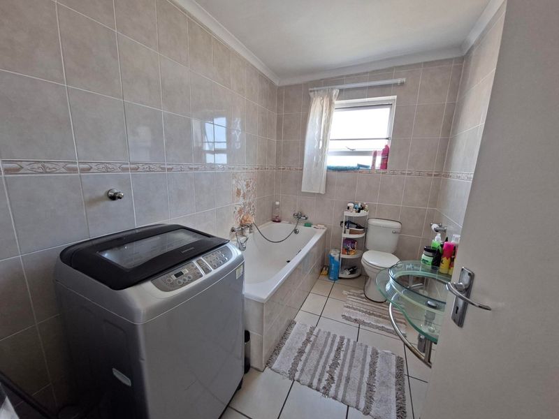 A functional bathroom featuring a bathtub, toilet, and glass basin with neutral ceramic wall and floor tiling.
