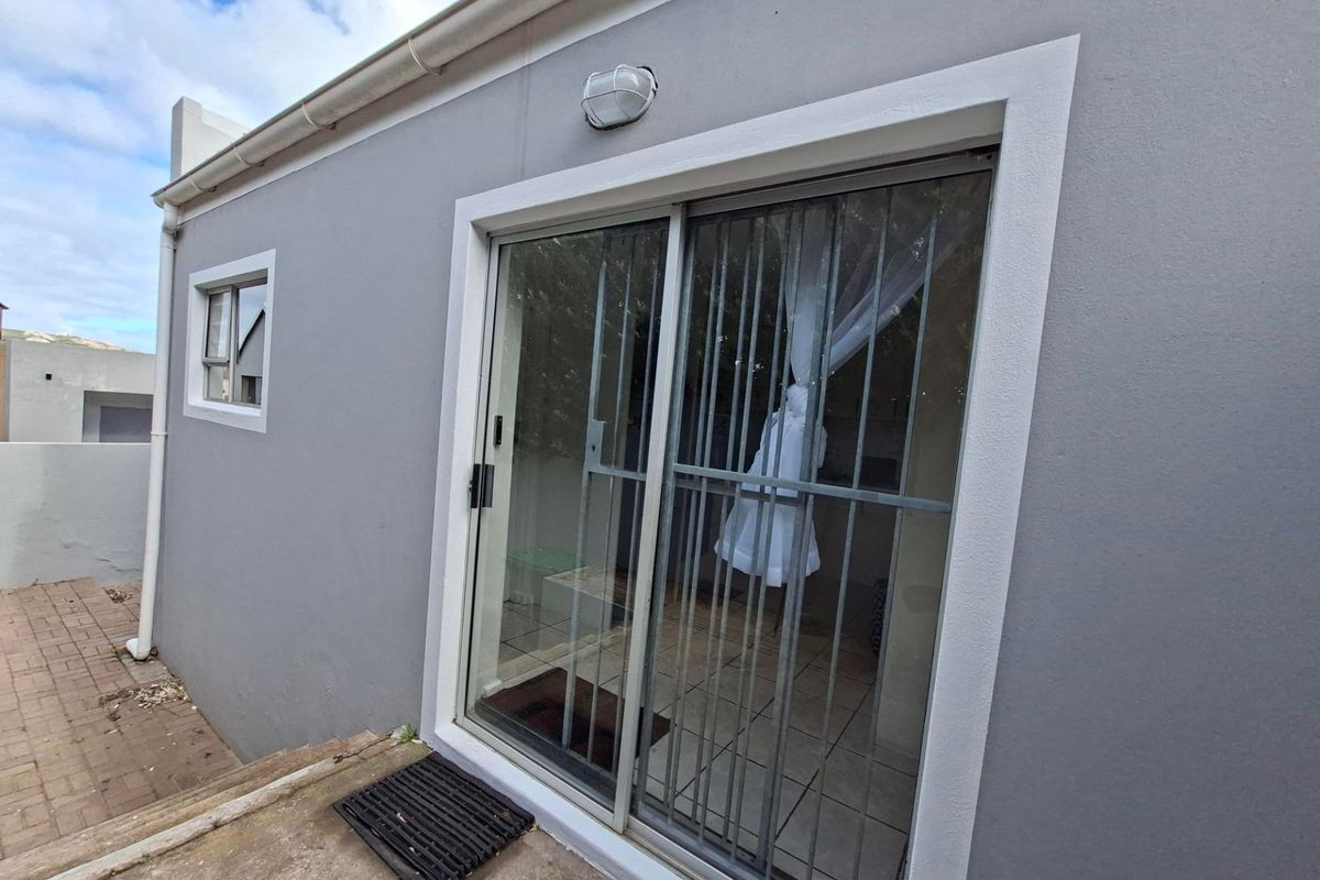 Rear exterior view of the apartment featuring a sliding glass door with security gate, paved patio area, and exterior wall lighting.