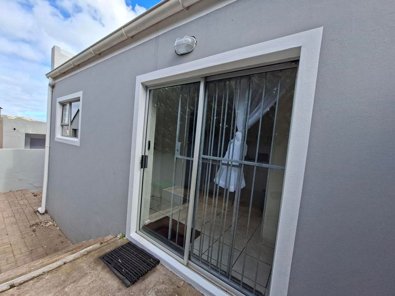 Rear exterior view of the apartment featuring a sliding glass door with security gate, paved patio area, and exterior wall lighting.