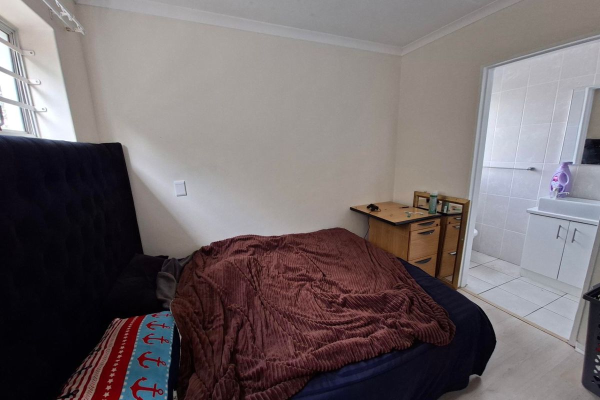 A bedroom featuring laminate flooring, coving, and an adjoining en-suite bathroom with tiled finishes.