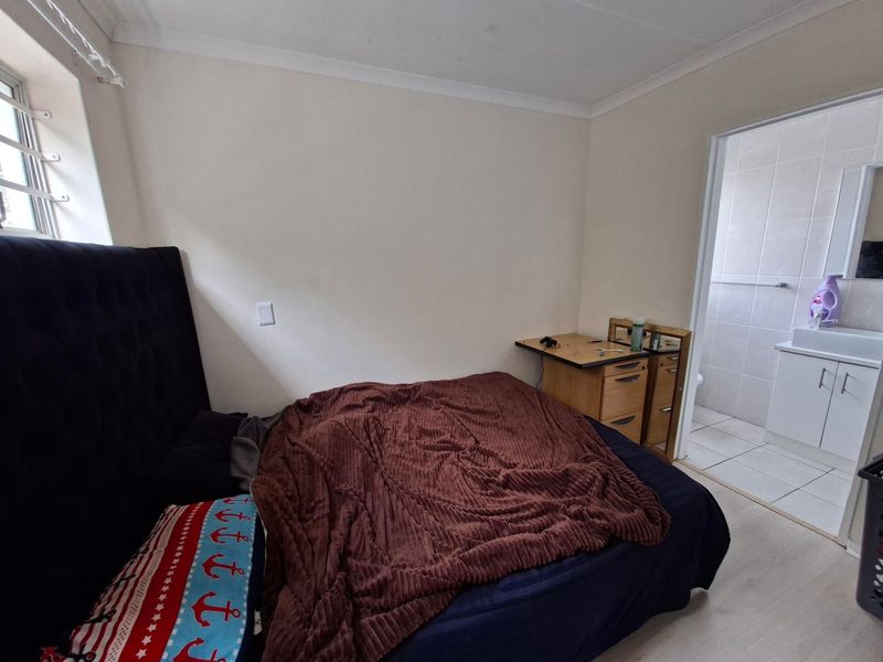 A bedroom featuring laminate flooring, coving, and an adjoining en-suite bathroom with tiled finishes.
