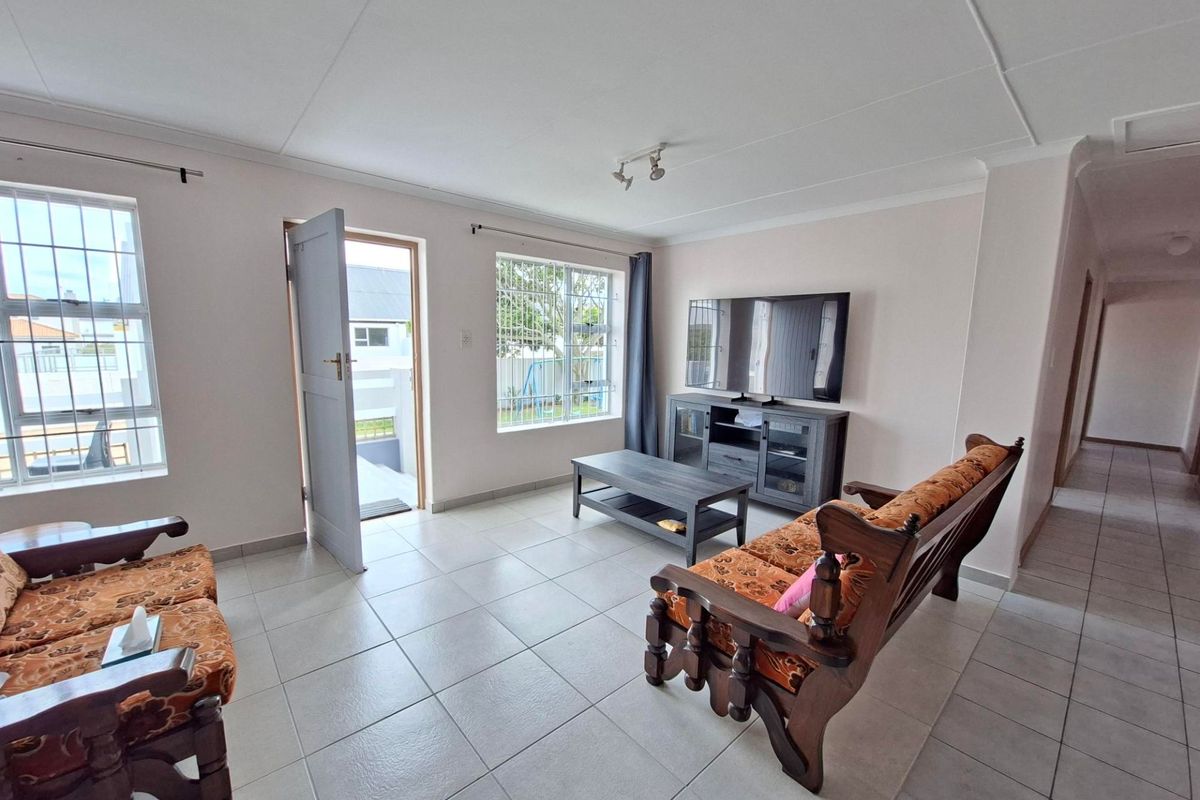 A bright living room featuring neutral tiled flooring, security bars on windows, and direct access to the exterior.