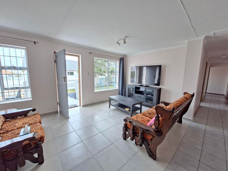 A bright living room featuring neutral tiled flooring, security bars on windows, and direct access to the exterior.