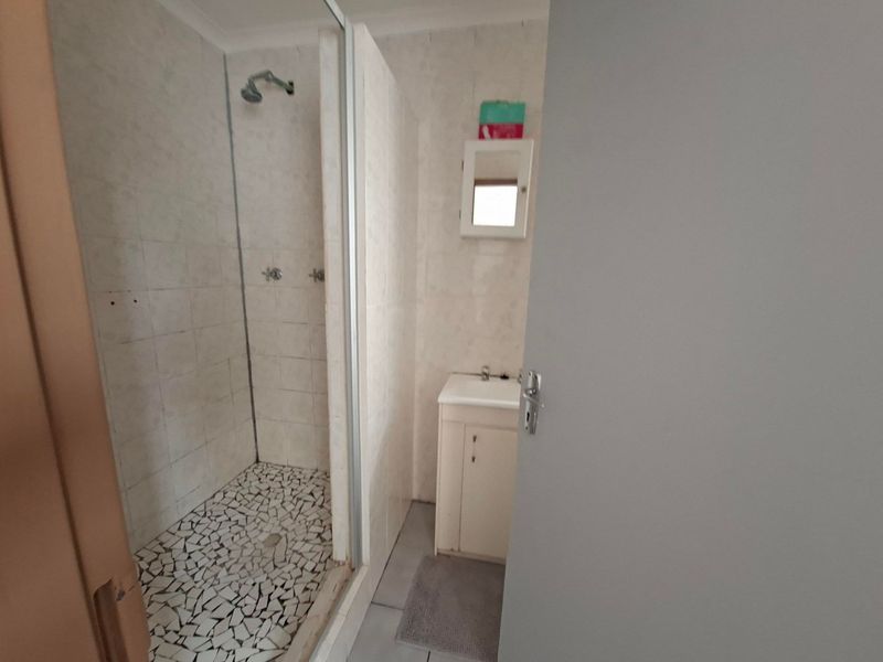 A functional bathroom featuring a walk-in shower enclosure with tiled flooring and a vanity basin unit.