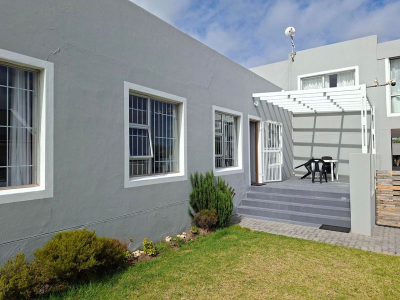 Rear exterior view featuring a paved patio area with a white pergola, security-fitted windows, and a small garden space.