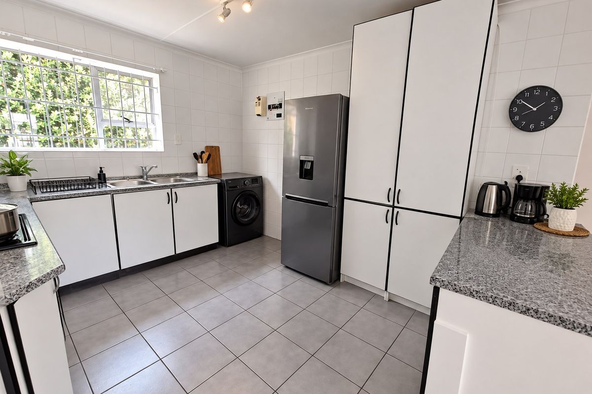 A clean and functional kitchen featuring granite countertops, white cabinetry, tiled walls and flooring, and a double sink with security bars on the window.