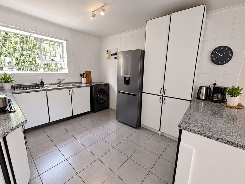 A clean and functional kitchen featuring granite countertops, white cabinetry, tiled walls and flooring, and a double sink with security bars on the window.
