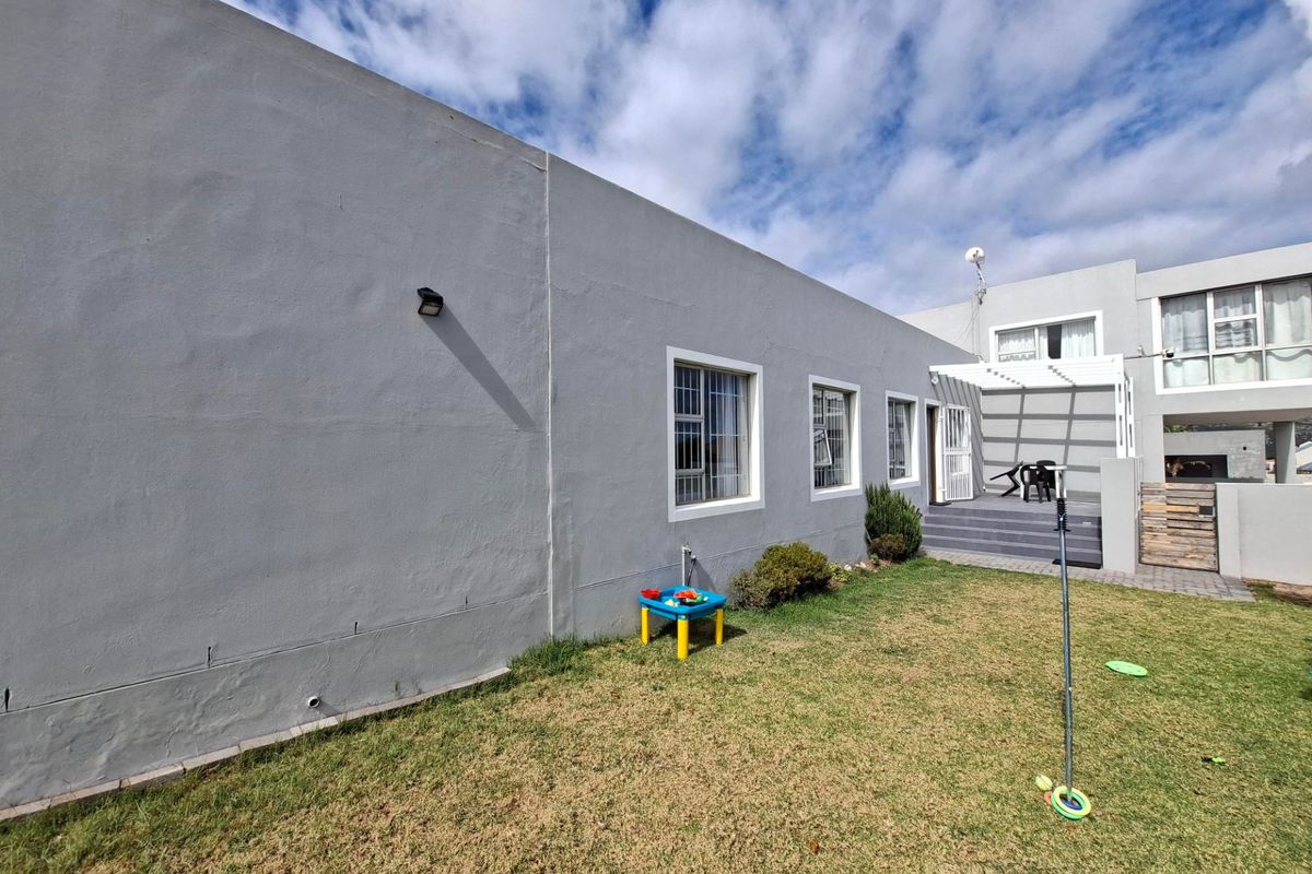 Rear exterior view of the property featuring a paved patio area with a pergola, security-barred windows, and a private lawn.