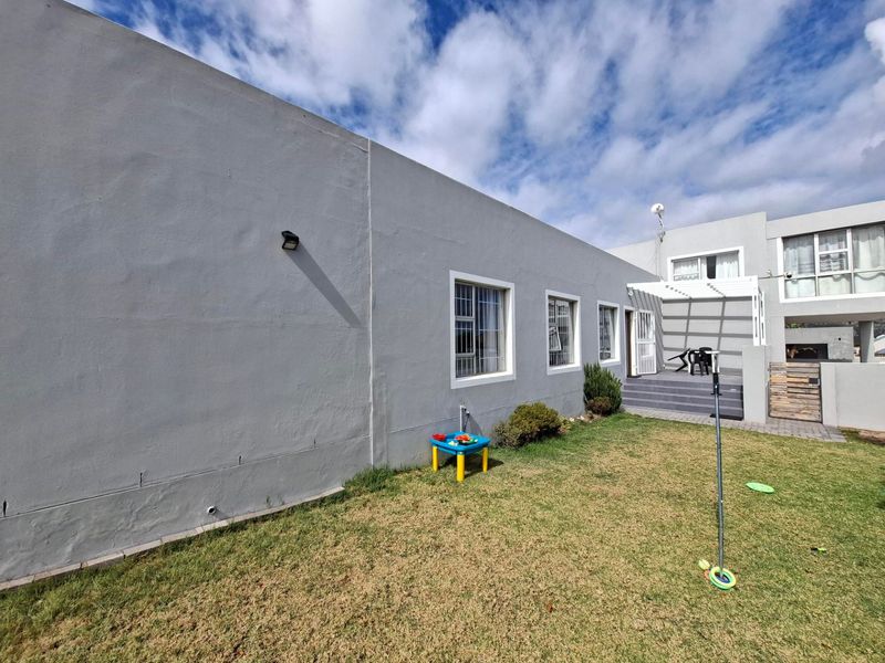 Rear exterior view of the property featuring a paved patio area with a pergola, security-barred windows, and a private lawn.