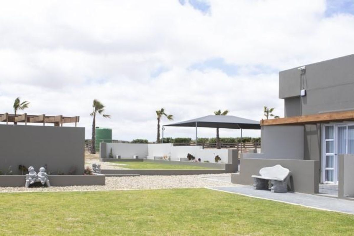 A well-maintained rear exterior view featuring a landscaped garden, paved pathways, a covered patio area, and modern grey rendered building walls.