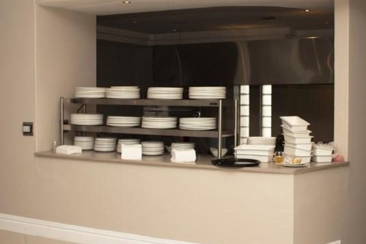 A service counter or pass-through area featuring a stainless steel shelving unit, recessed ceiling lighting, and tiled flooring.