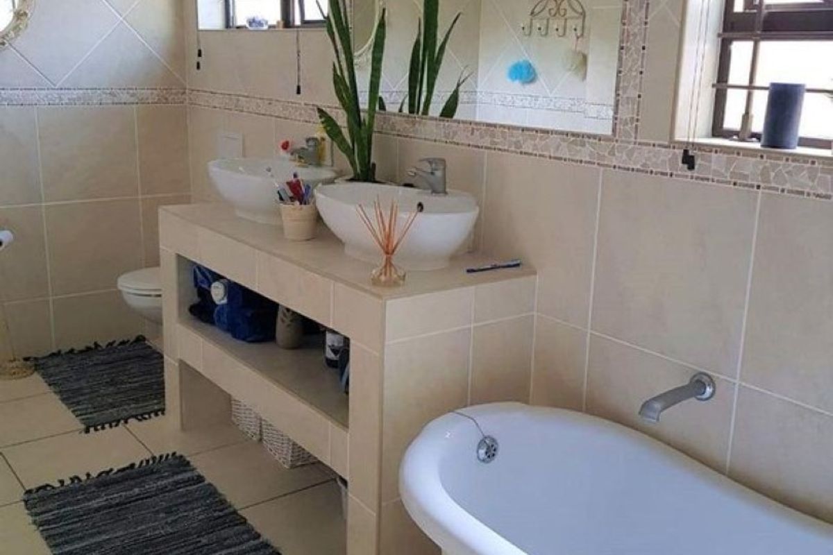 A bathroom featuring a double vanity with vessel sinks, a freestanding clawfoot bathtub, tiled walls, and large wall-mounted mirrors.