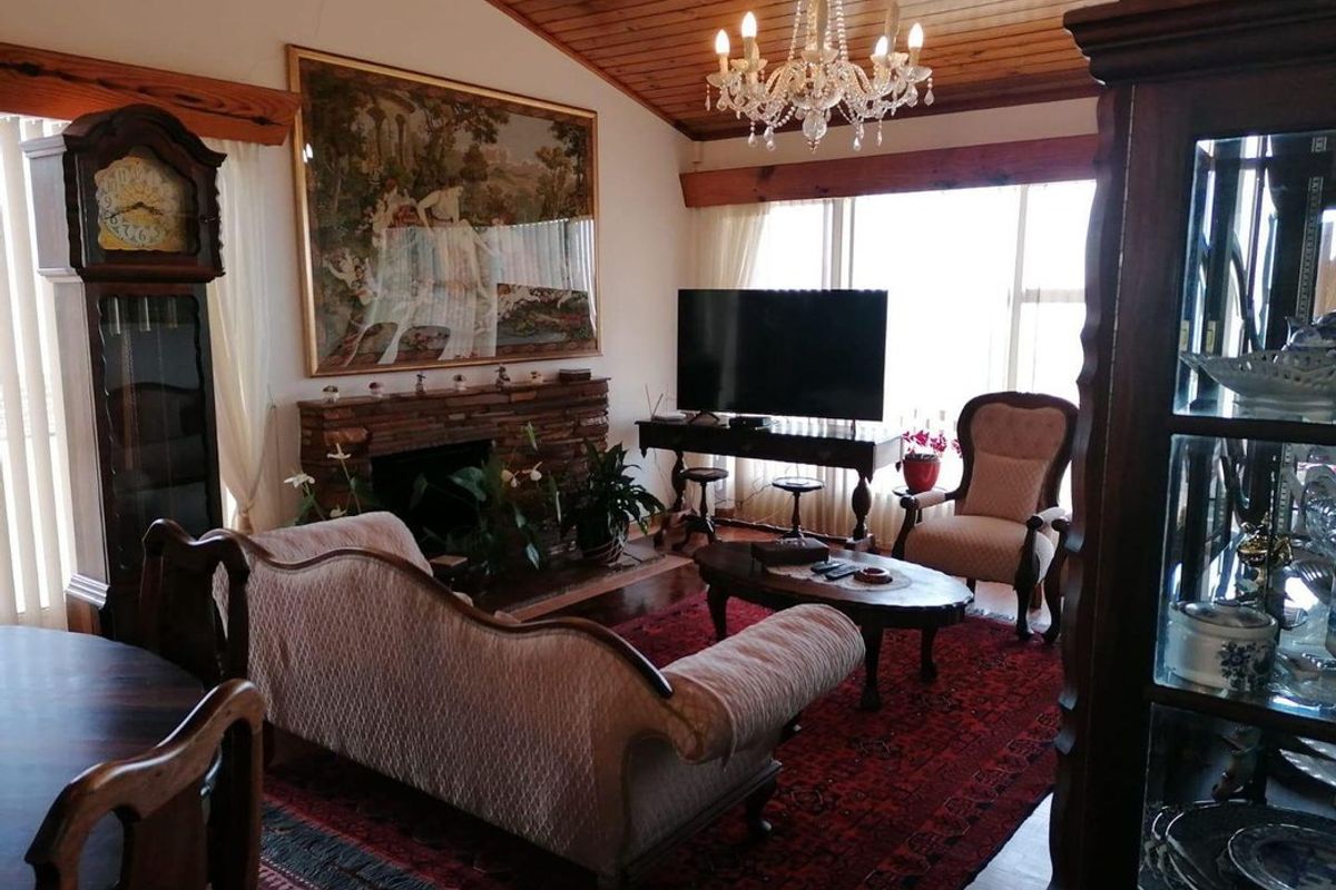 A cozy living room featuring a brick fireplace, vaulted timber-paneled ceiling, and large windows providing natural light.