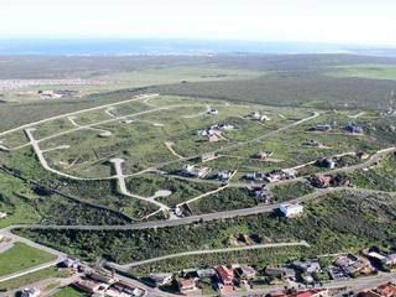 An aerial view of a residential development site featuring established road infrastructure and multiple vacant plots set within a coastal landscape.