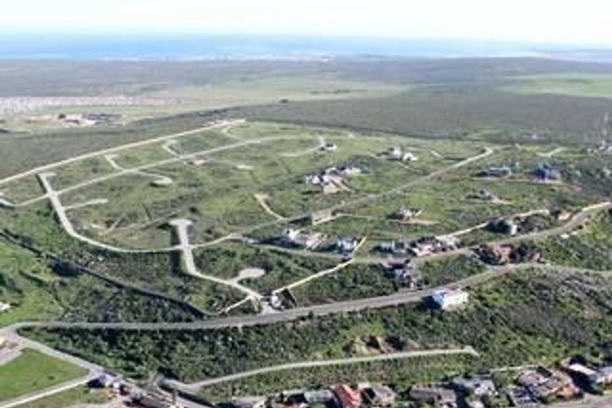 An aerial view of a residential development site featuring established road infrastructure and multiple vacant plots set within a coastal landscape.