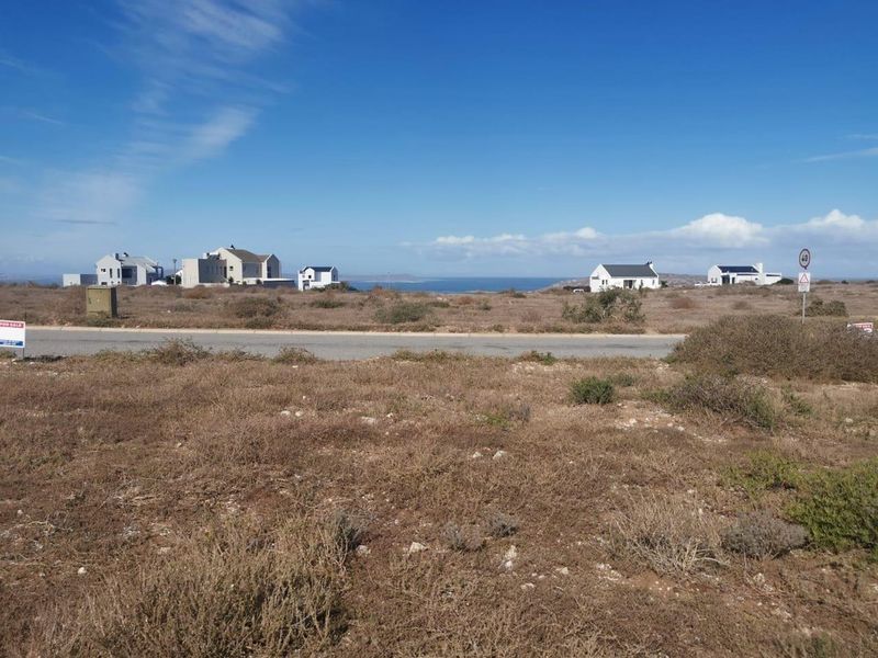 A view of a vacant residential plot featuring coastal landscape and distant ocean views, situated along a paved road.
