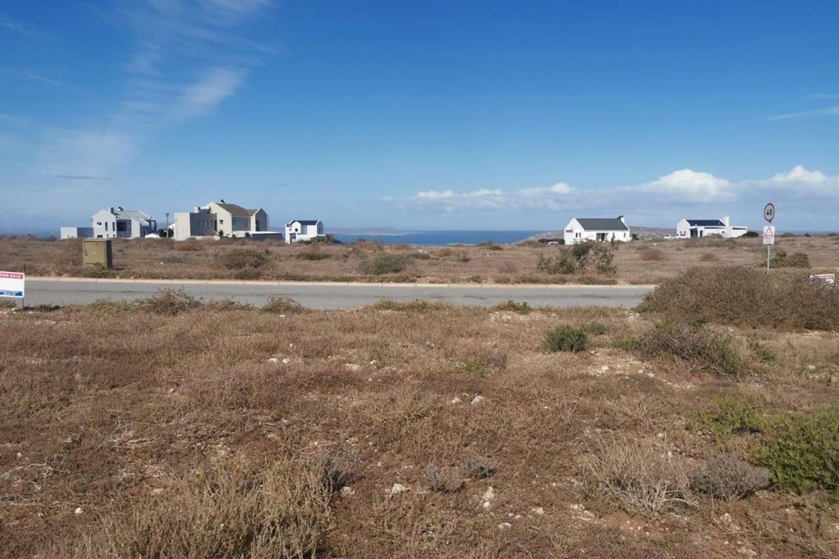 A view of a vacant residential plot featuring coastal landscape and distant ocean views, situated along a paved road.