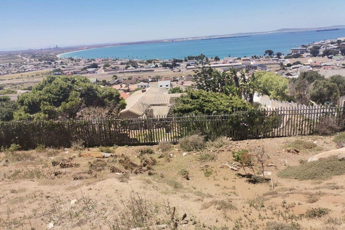 Elevated view overlooking the coastal town and bay, featuring natural terrain and perimeter fencing.
