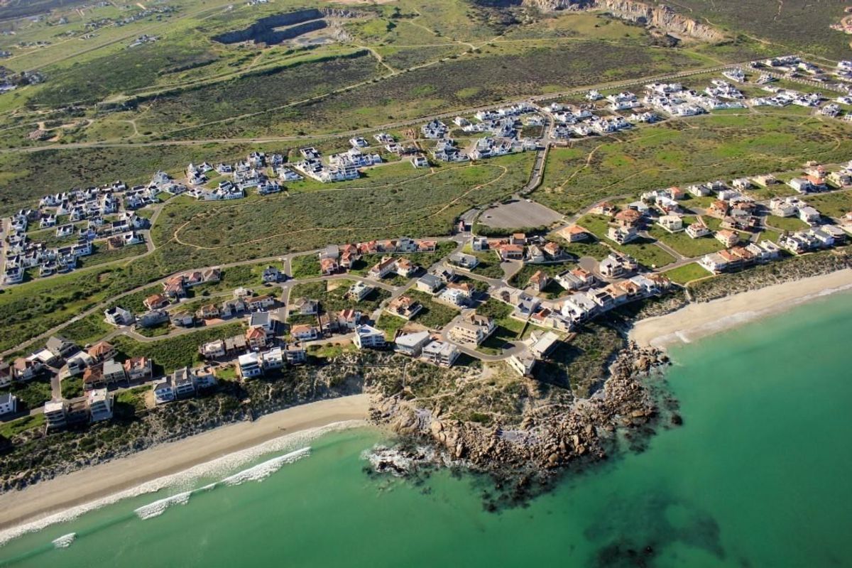 Aerial view of a coastal residential estate featuring established homes, paved road networks, and direct access to a sandy beach and rocky shoreline.