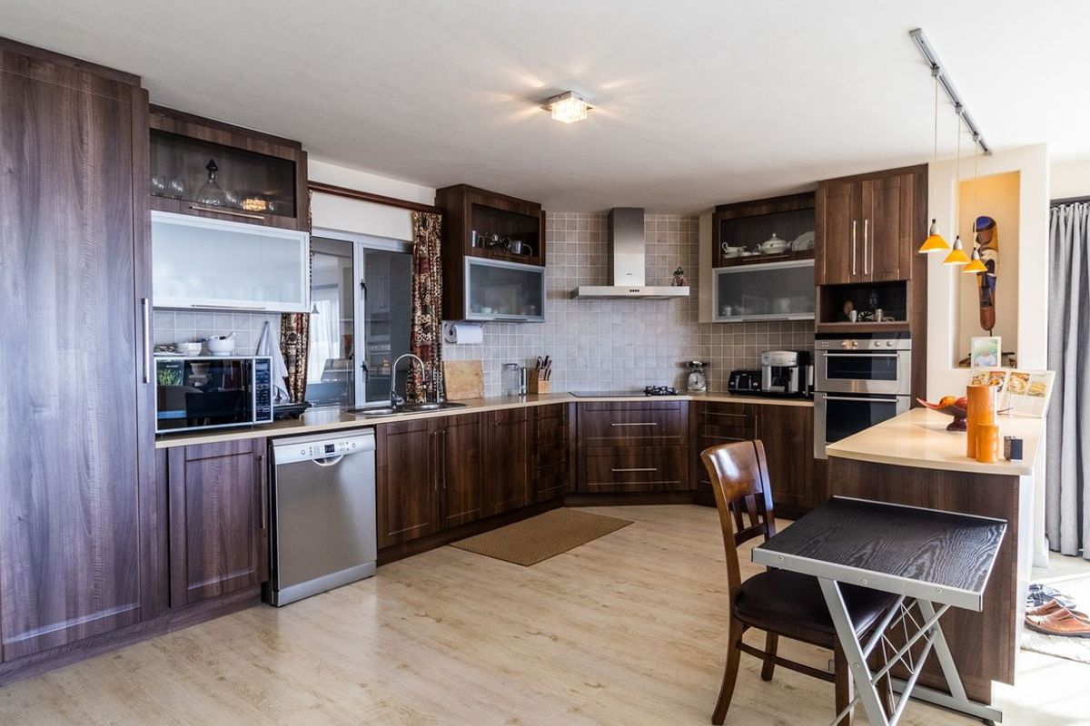 A well-appointed kitchen featuring dark wood cabinetry, integrated stainless steel appliances, a tiled backsplash, and a functional breakfast bar island.