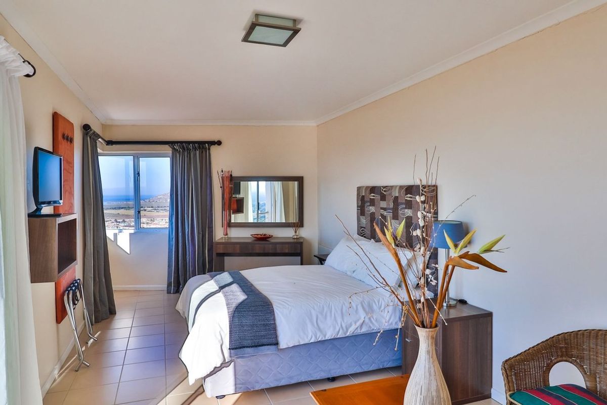 A bright bedroom featuring tiled flooring, a large window with scenic views, and a built-in wall-mounted shelf unit.