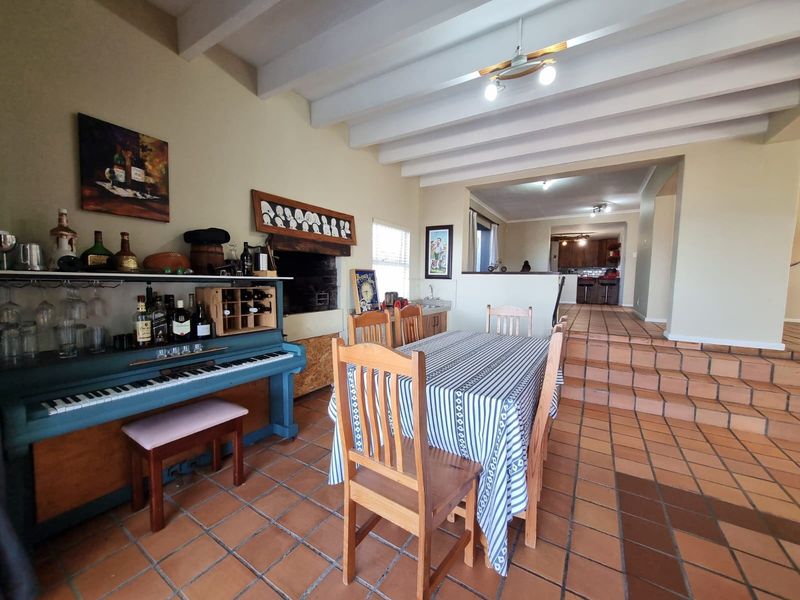 Open plan dining area featuring terracotta floor tiles, exposed ceiling beams, and a built-in fireplace, with steps leading to the adjacent kitchen.