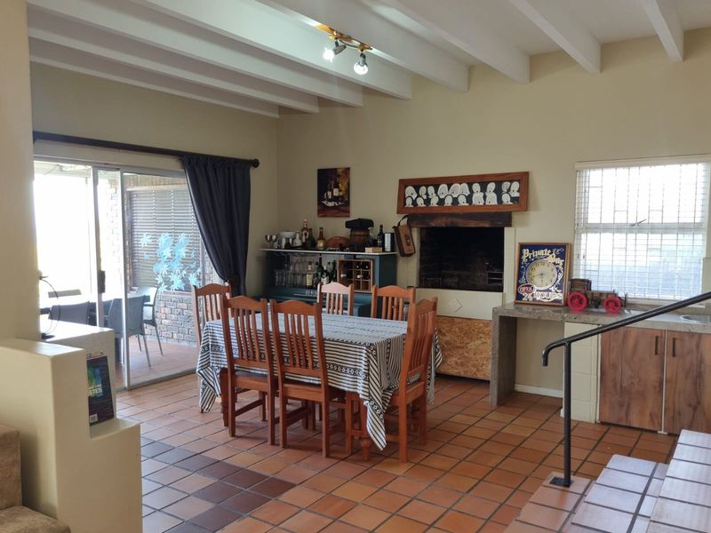 Open-plan dining area featuring exposed beam ceilings, built-in indoor braai, and direct access to the patio through sliding glass doors.