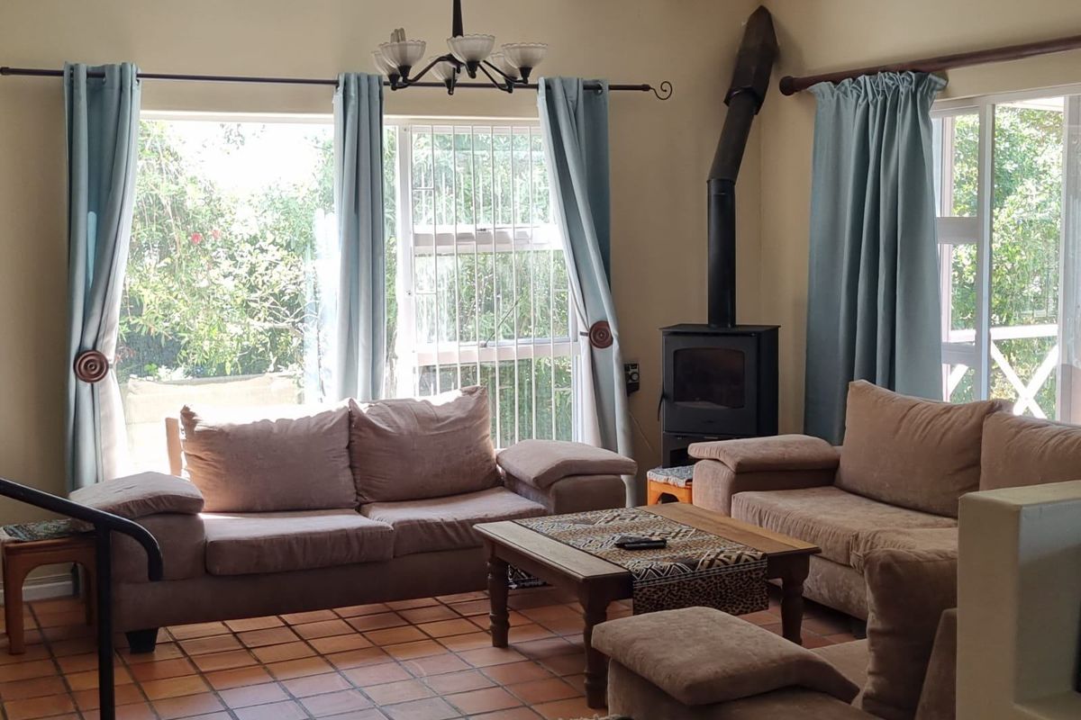 A cozy living room featuring terracotta floor tiles, a built-in wood-burning fireplace, and large windows providing natural light and garden views.