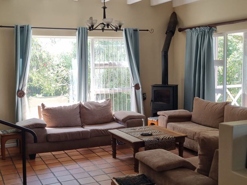 A cozy living room featuring terracotta floor tiles, a built-in wood-burning fireplace, and large windows providing natural light and garden views.
