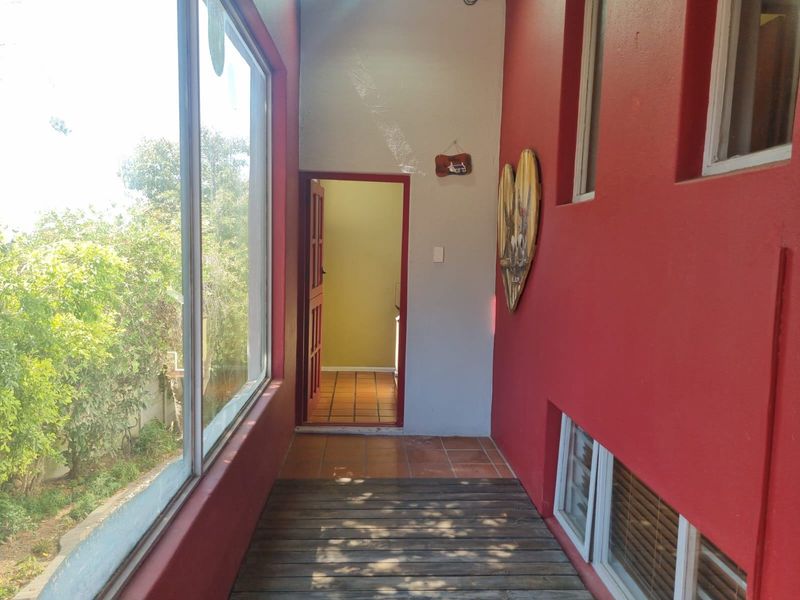 A covered patio area featuring wooden decking, large windows overlooking the garden, and access to the interior of the home.