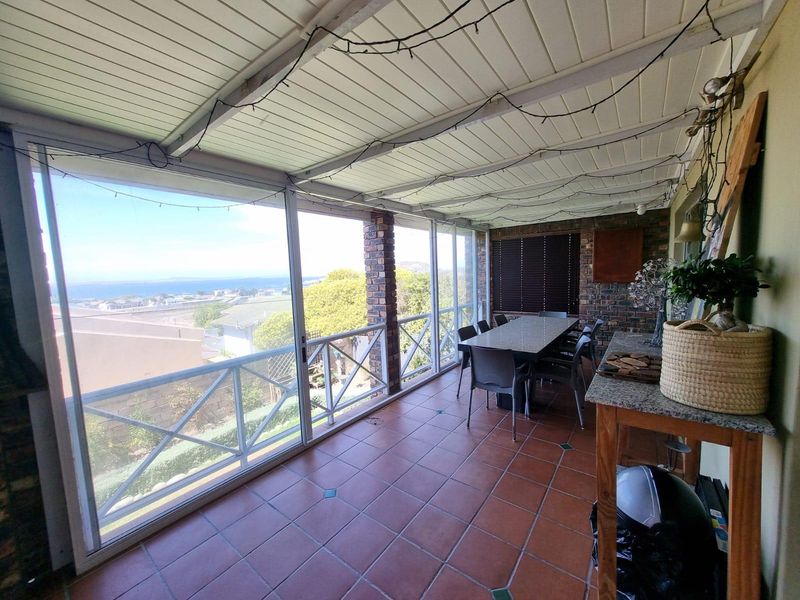Enclosed patio area featuring tiled flooring, brick accents, and large windows offering expansive coastal views, ideal for outdoor dining and relaxation.