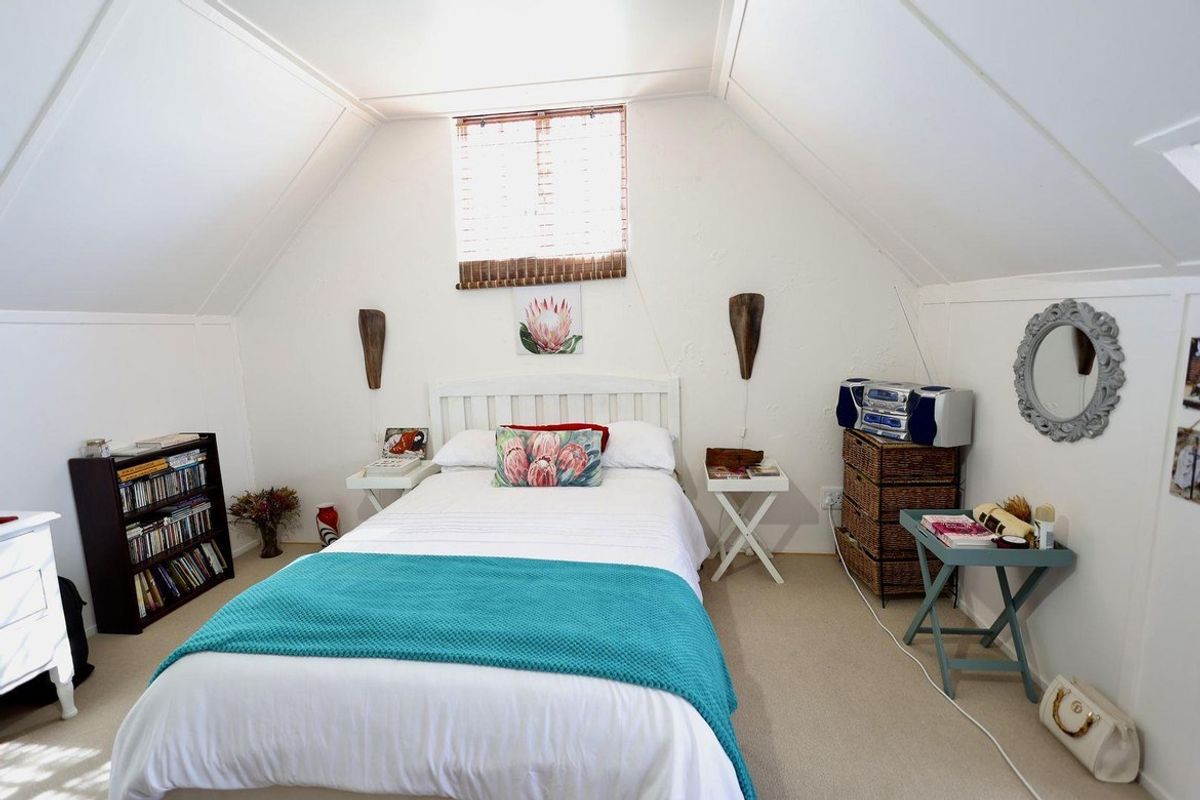 A cozy bedroom featuring sloped ceilings, neutral carpeting, and a window with fitted blinds, creating a comfortable and functional sleeping space.