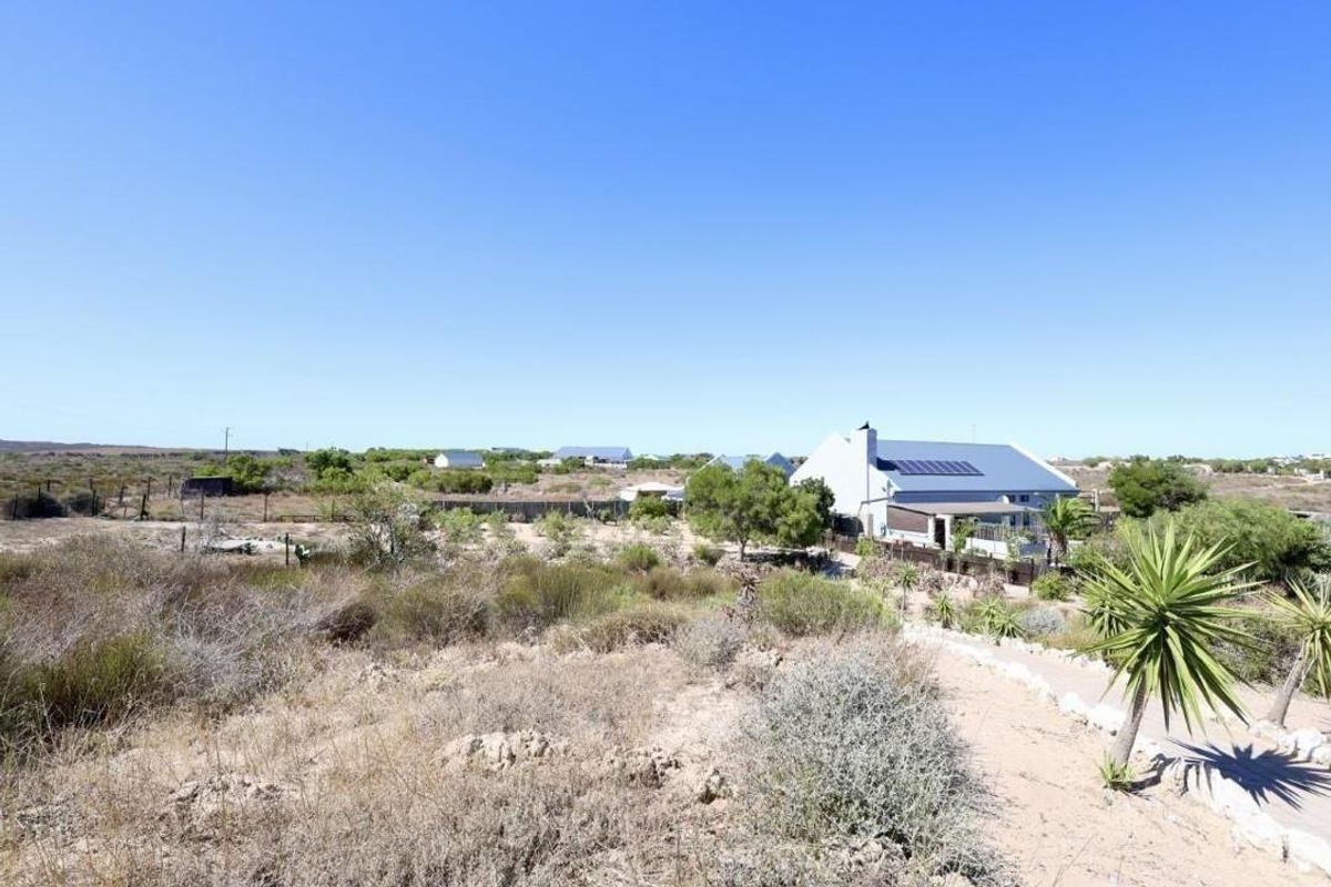 An elevated view of the property showing the house exterior, roof-mounted solar panels, and the surrounding natural landscape and garden area.