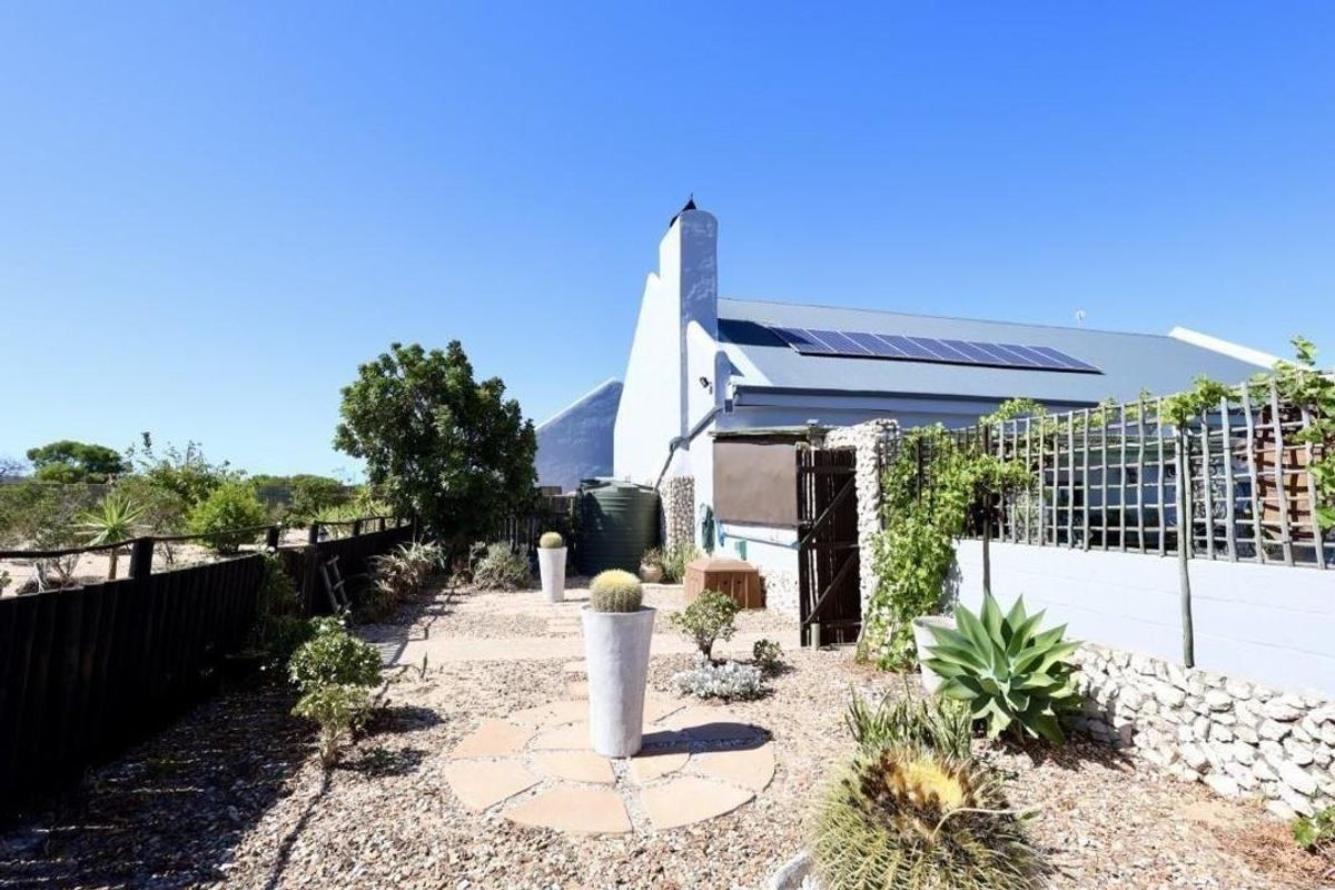 A rear garden area featuring a gravel landscape, stone retaining wall, water tank, and solar panels installed on the roof.