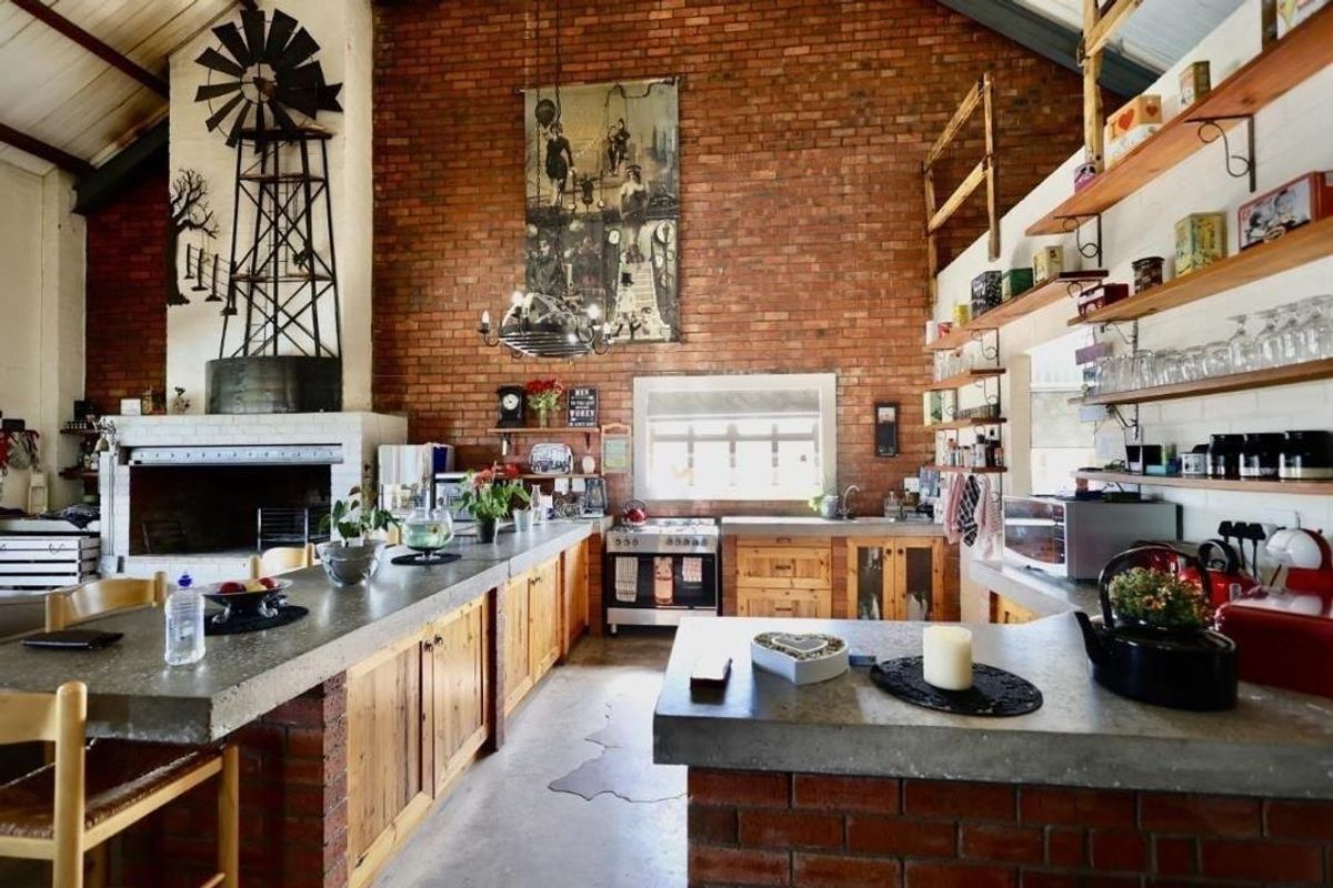 Spacious rustic kitchen featuring exposed brick walls, concrete countertops, wooden cabinetry, and a large built-in fireplace with a decorative windmill feature.