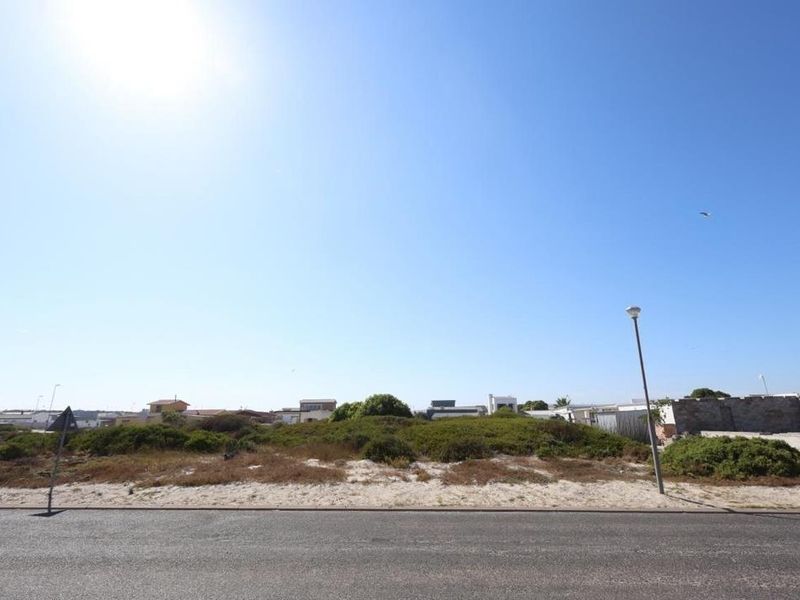 A view of a vacant residential plot featuring natural coastal vegetation, adjacent to a paved road with existing street lighting.