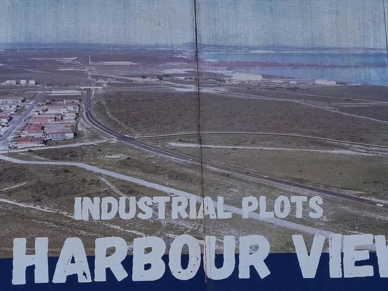 A large outdoor billboard displaying an aerial view of industrial plots and harbour surroundings, showing significant signs of weathering and wear.