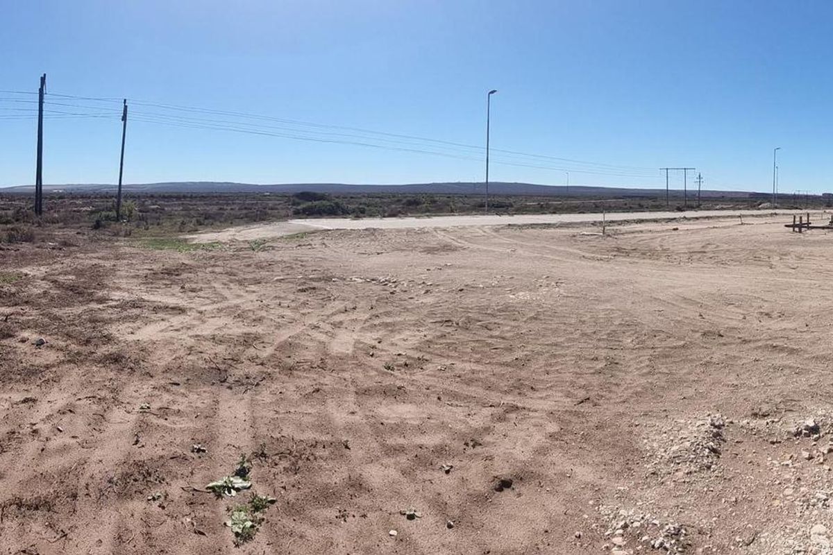 A wide panoramic view of an undeveloped commercial plot featuring dirt terrain, utility poles, and distant horizon lines under a clear sky.